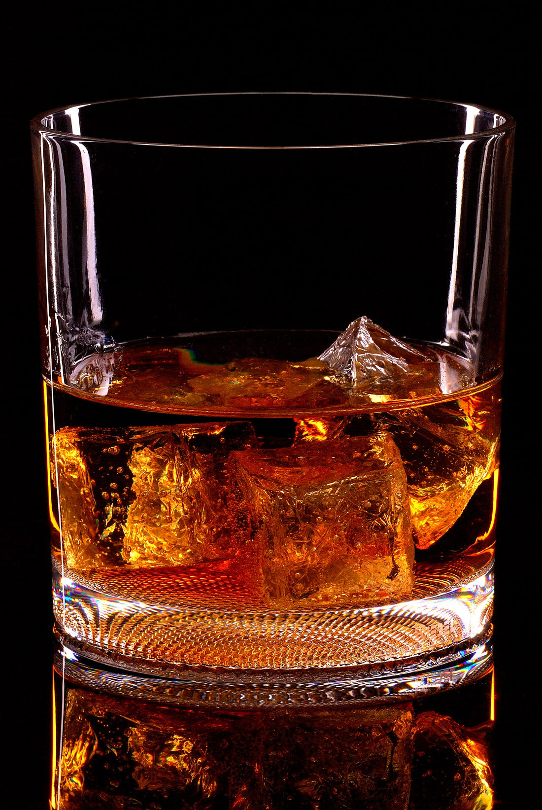 A cold amber drink over ice in a glass against a black background