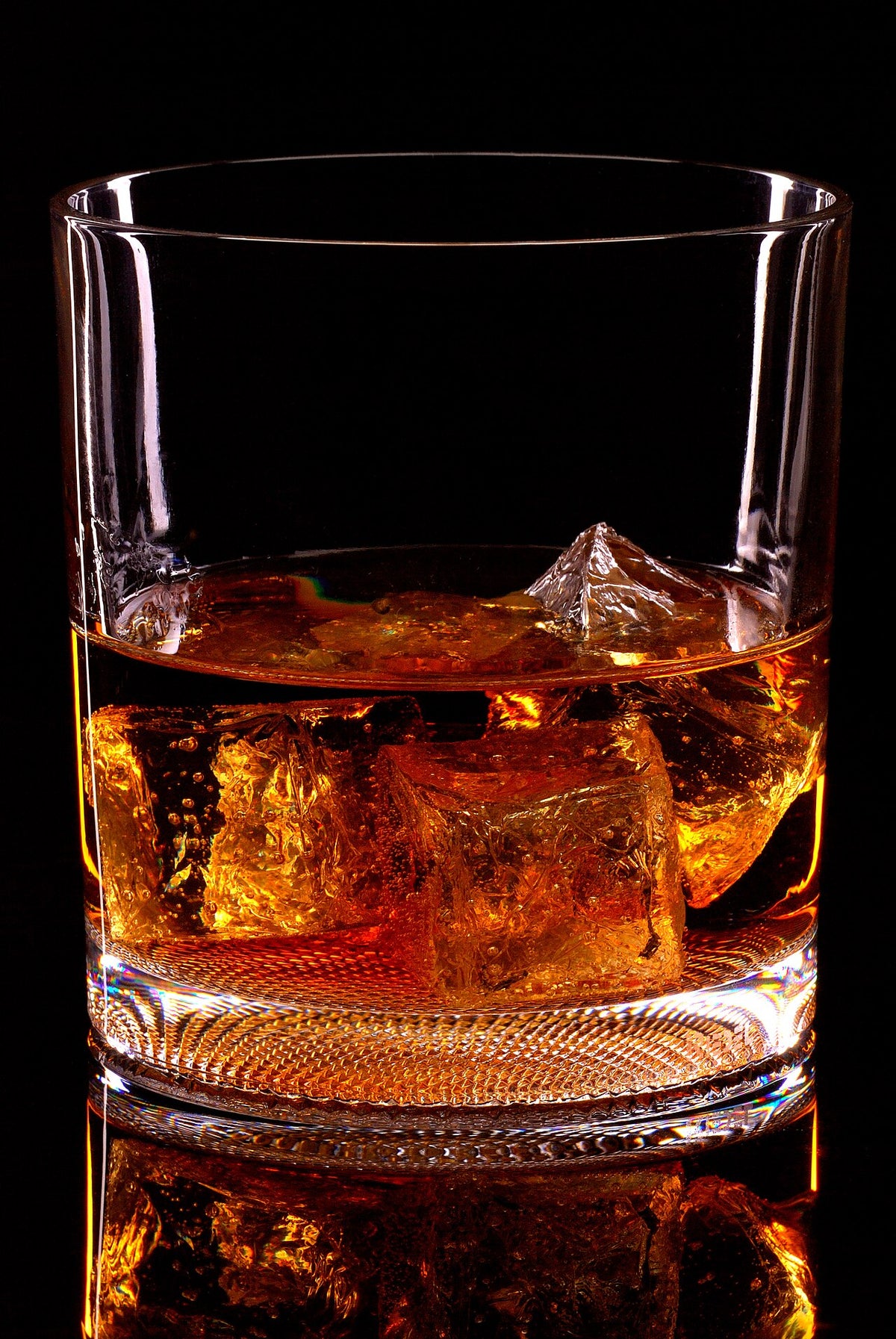 A cold amber drink over ice in a glass against a black background