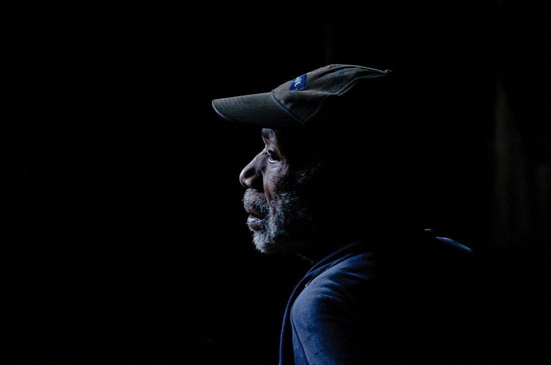 Older man with a grey beard in profile against a black background