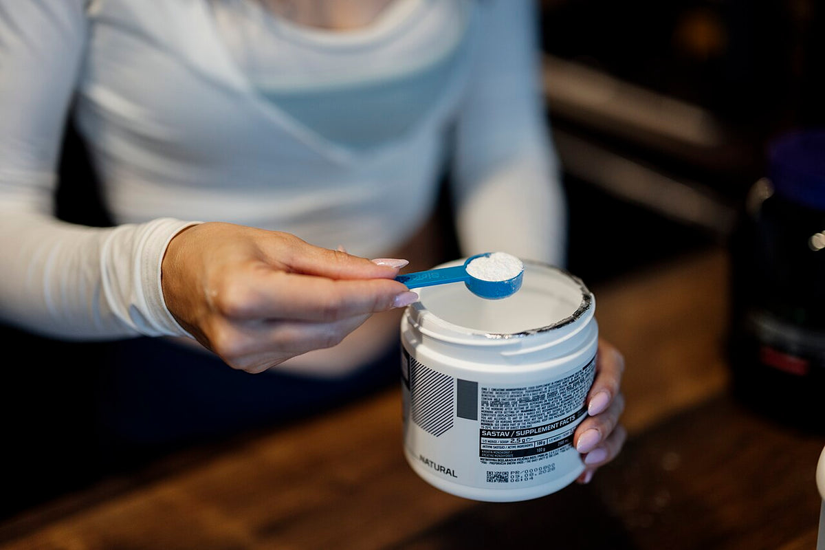 Scoop of white amino acid powder held over an open supplement tub