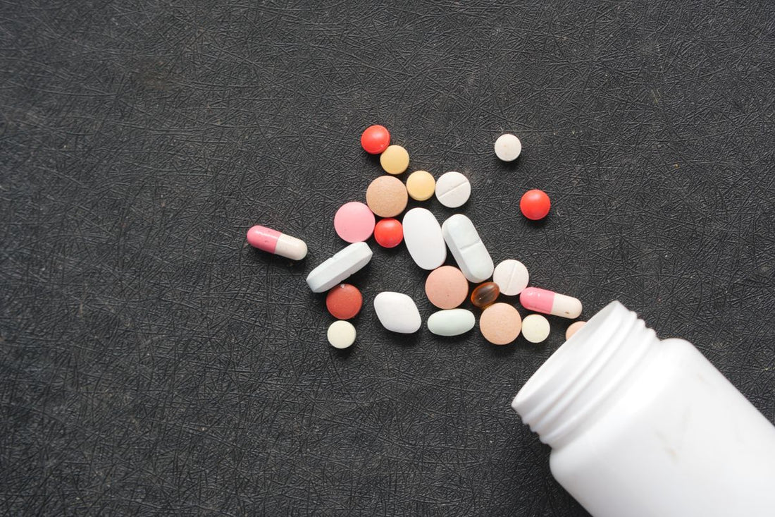 Multivitamin pills spilled from a white bottle on a dark surface