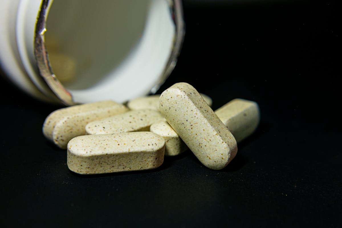 Speckled multivitamin tablets spilling from a white bottle on a black background