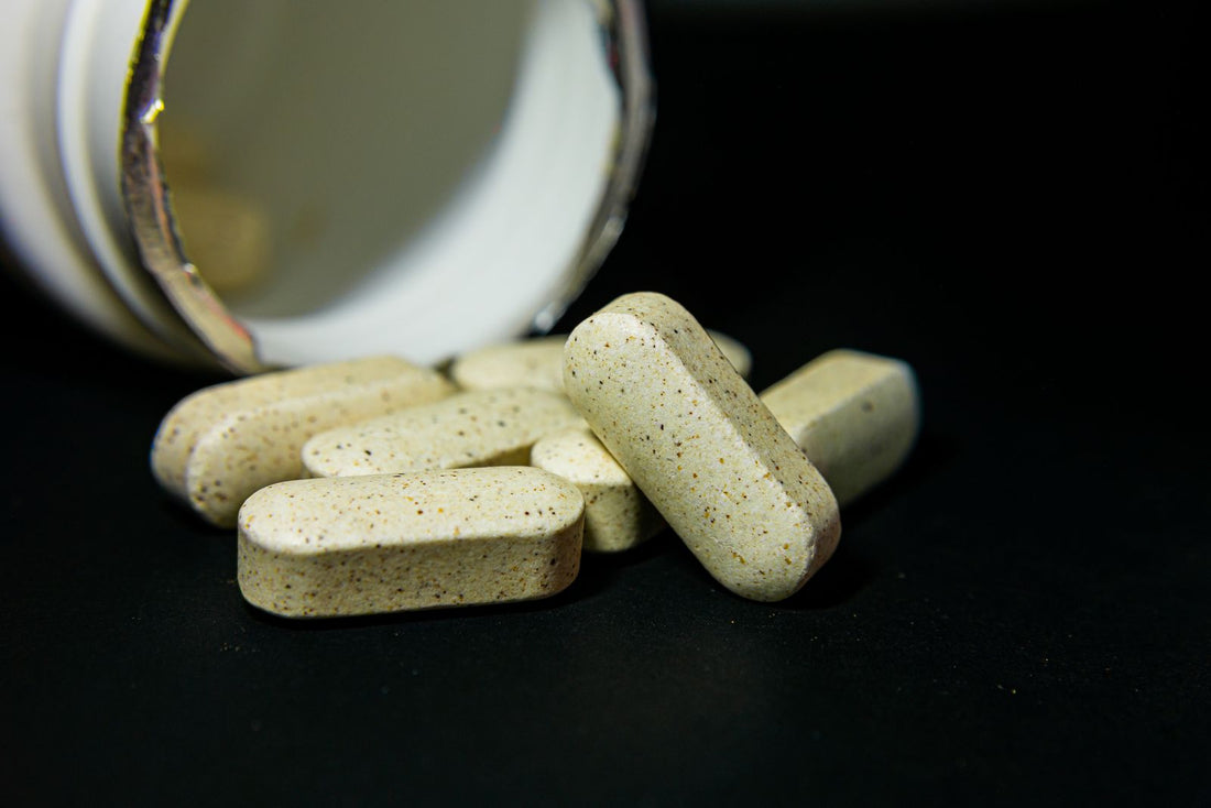 Supplement tablets spilling from a bottle onto a dark surface