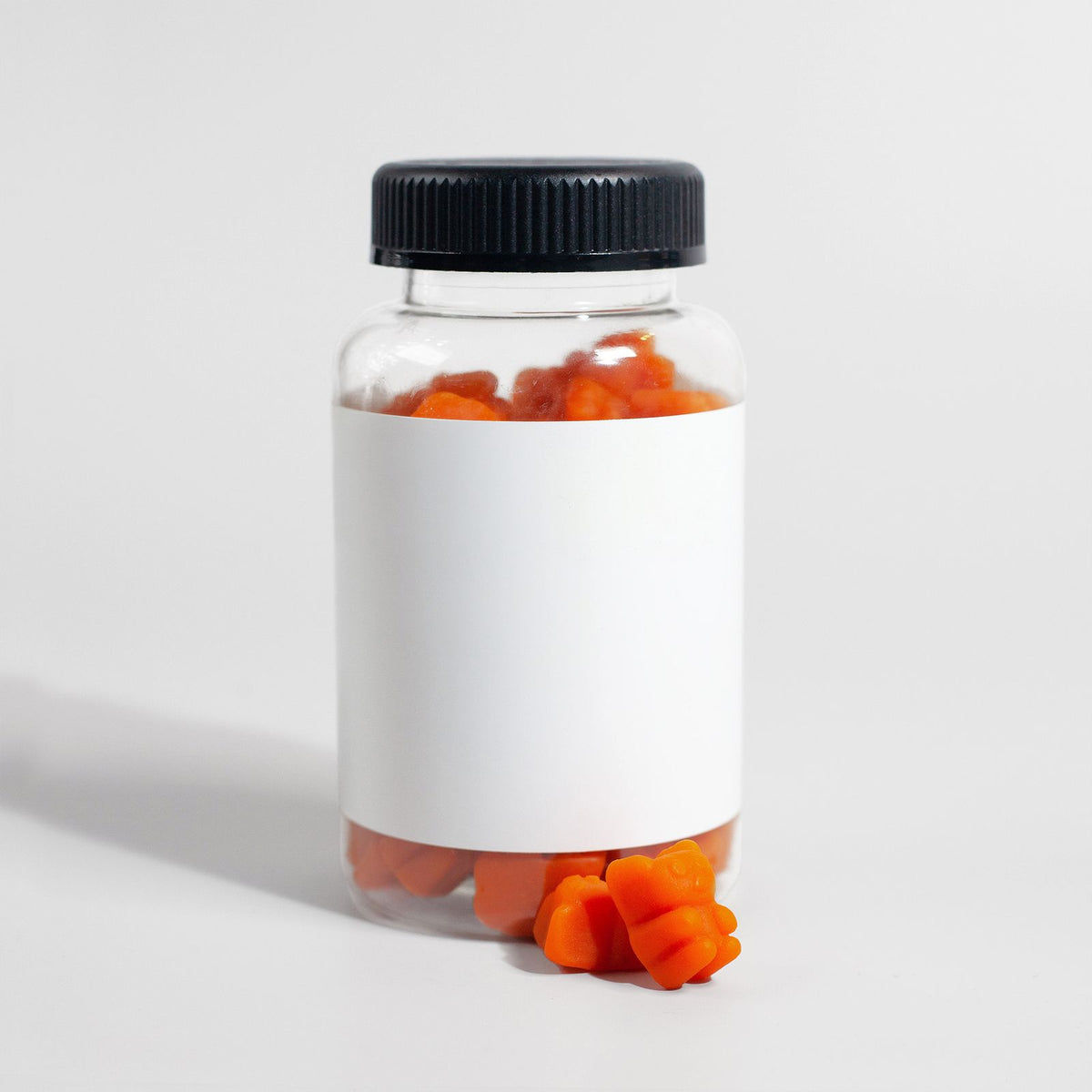 A clear supplement bottle of orange gummies with a blank white label
