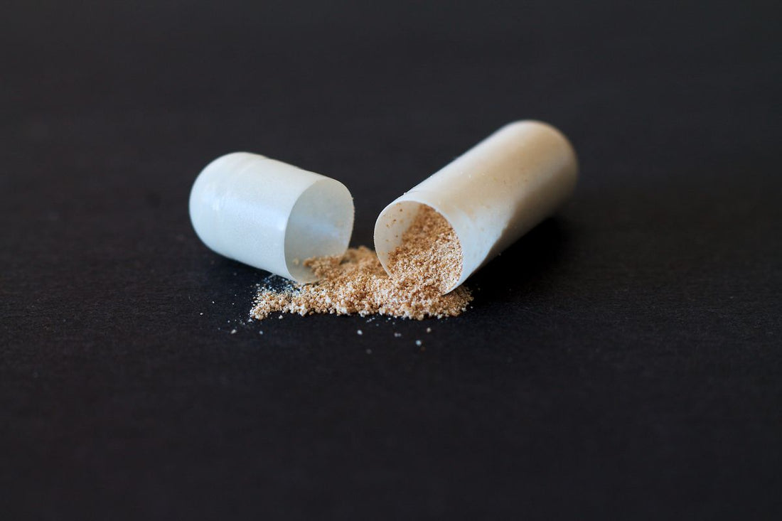 Opened supplement capsule spilling powder onto a dark surface