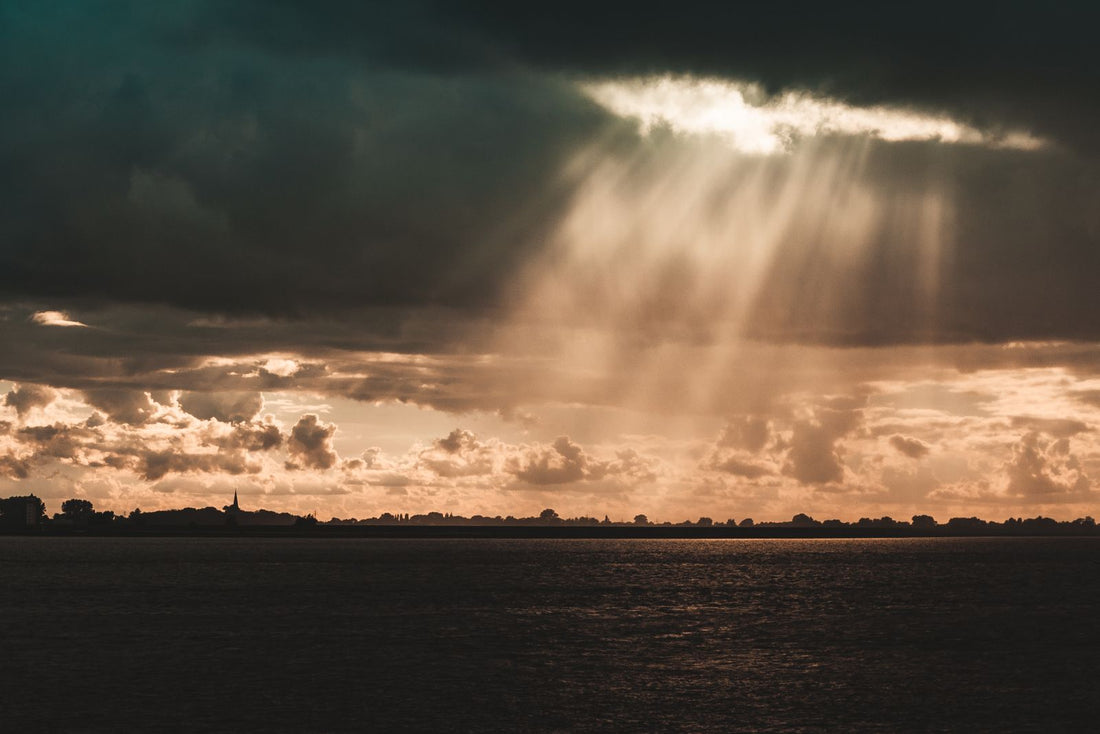 Sun rays breaking through dark storm clouds over water