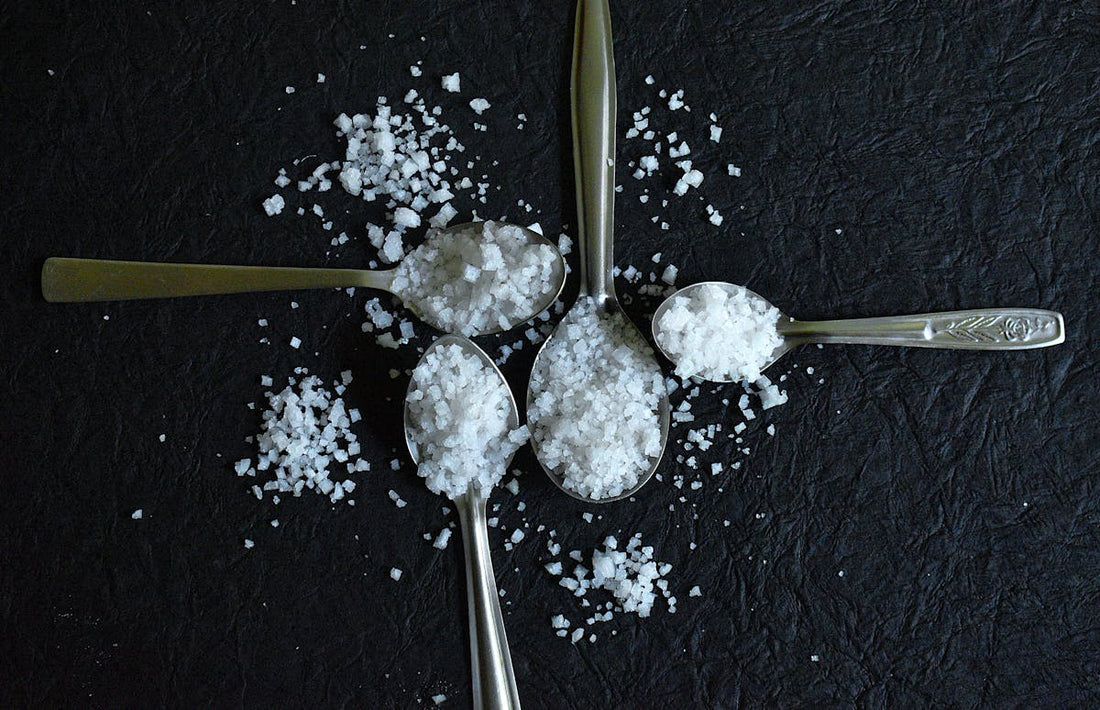 Coarse sea salt spilling from spoons on a dark surface