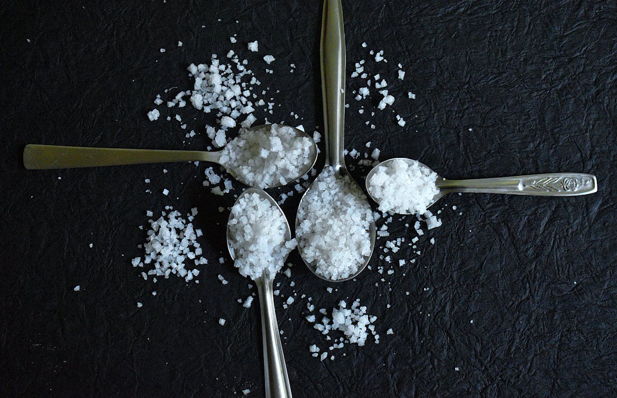 Coarse sea salt spilling from spoons on a dark surface