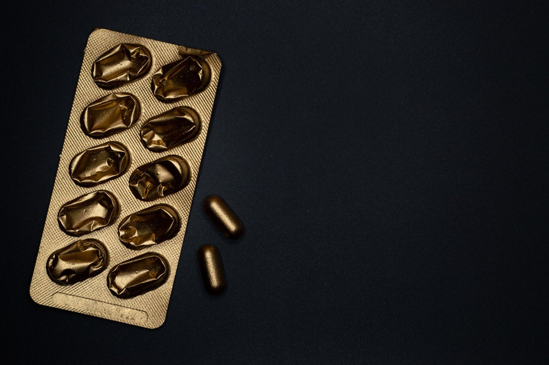 Gold blister pack and loose capsules on a black surface