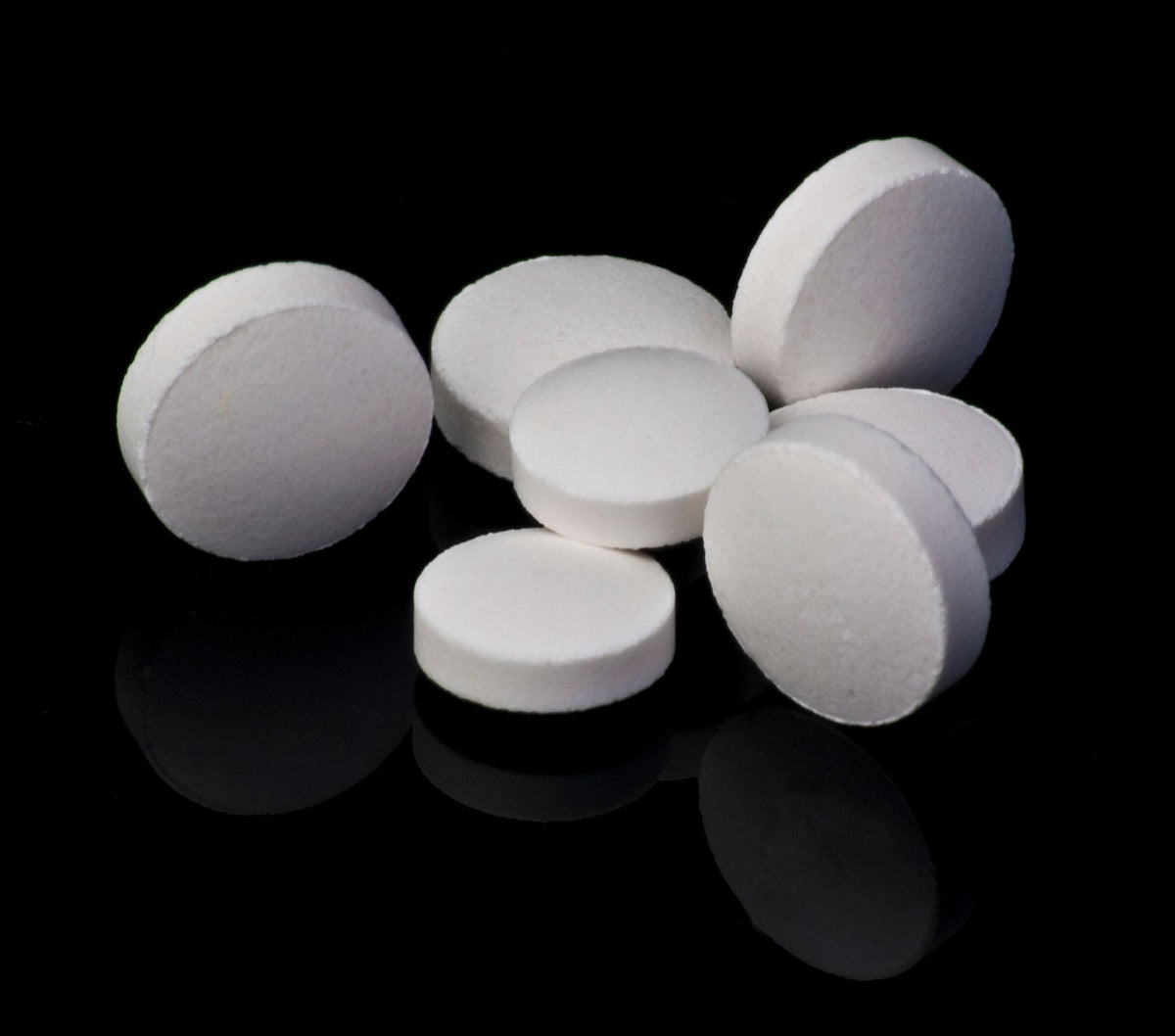 White calcium tablets on a black reflective surface