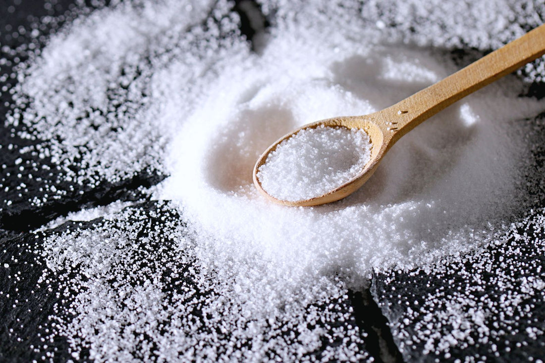 Coarse salt scattered across a dark slate surface with a wooden spoon