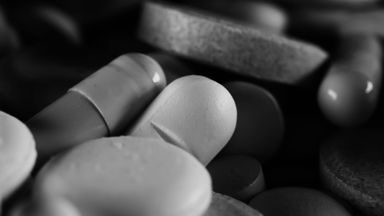 Dark macro shot of supplement capsules and tablets, black and white aesthetic