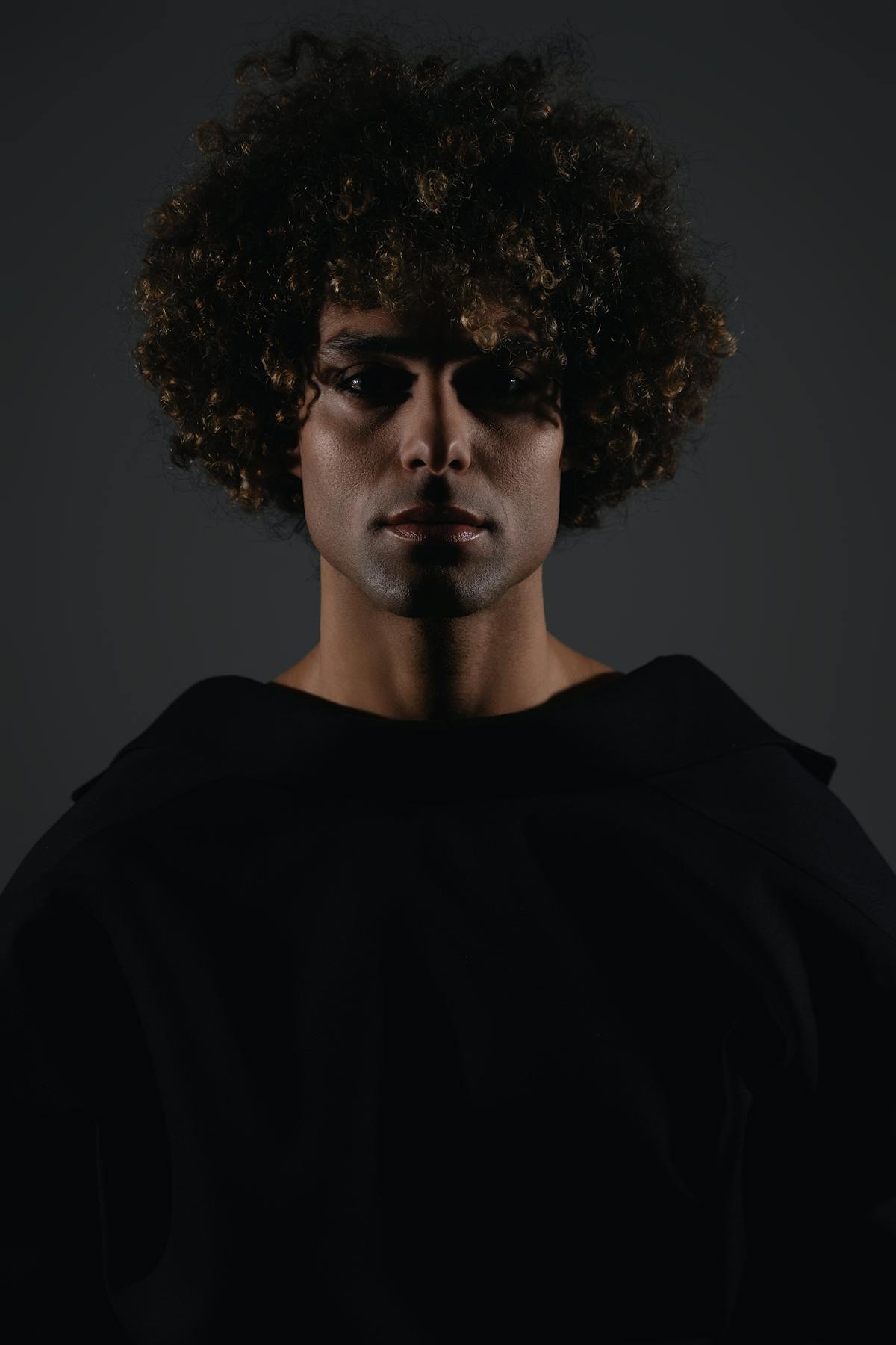 Dramatic male portrait with thick curly hair in low light, illustrating hair and skin nutrient symptoms