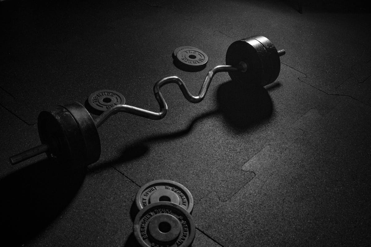 Dark gym floor with a loaded EZ curl bar and weight plates, low light, representing training while cutting