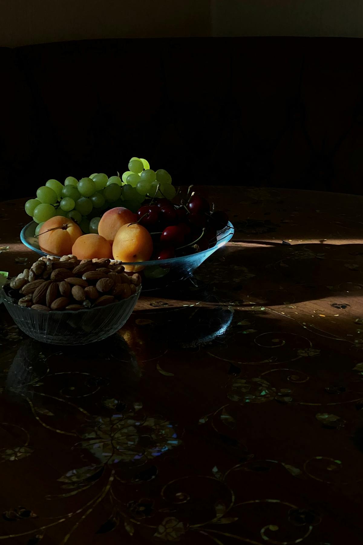 Bowl of almonds beside fruit on a dark table, a leading dietary source of vitamin E
